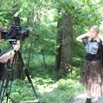 A performer in front of a camera in the woods